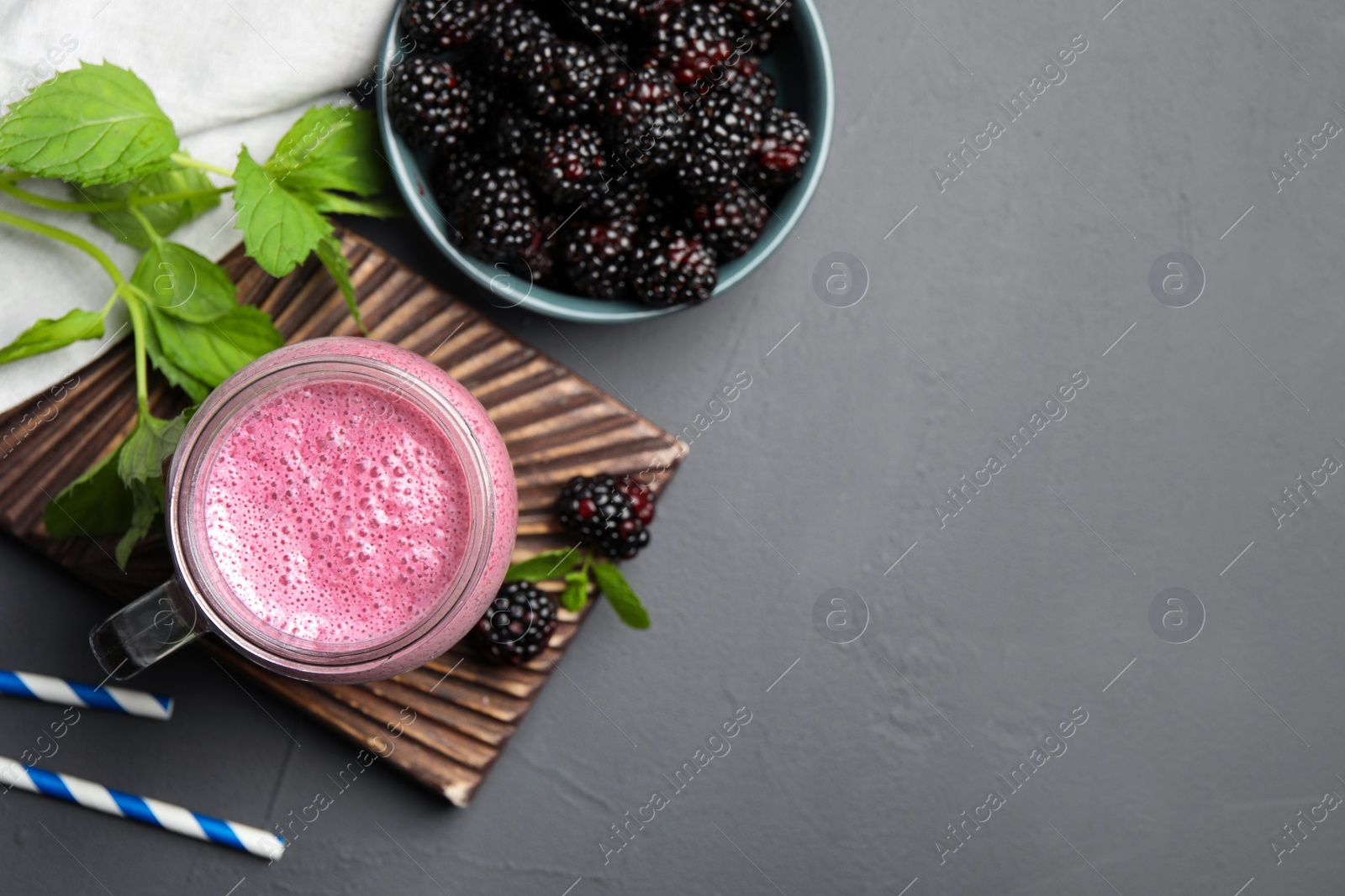 Photo of Mason jar of blackberry smoothie with mint and berries on grey table, flat lay. Space for text