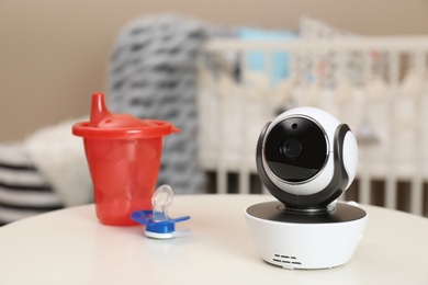 Photo of Modern CCTV security camera, baby cup and pacifier on table in nursery