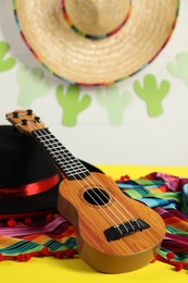 Black Flamenco hat, poncho and ukulele on yellow table, closeup