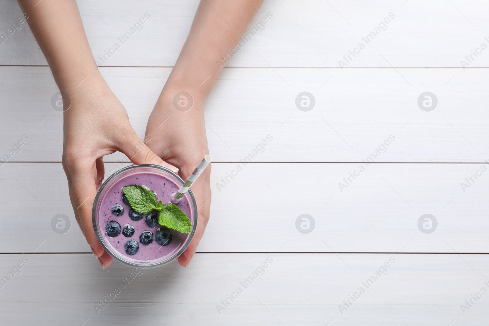 Photo of Woman with tasty blueberry smoothie at white wooden table, top view. Space for text