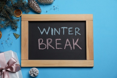 Photo of Chalkboard with words Winter Break and Christmas decor on light blue background, flat lay. School holidays