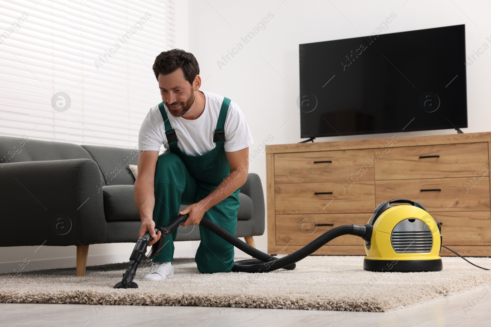 Photo of Dry cleaner's employee hoovering carpet with vacuum cleaner in room