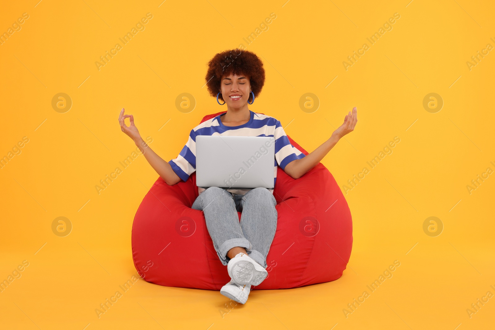 Photo of Young woman taking break from work on beanbag chair against orange background