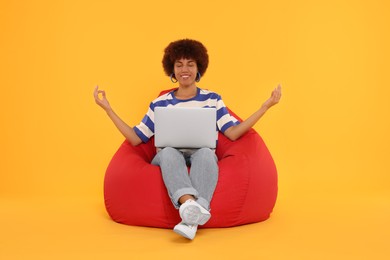 Photo of Young woman taking break from work on beanbag chair against orange background