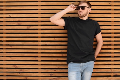 Photo of Young man wearing black t-shirt against wooden wall on street. Urban style