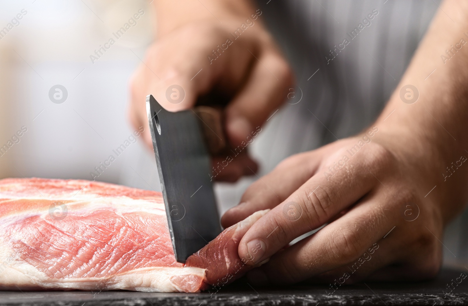 Photo of Man cutting fresh raw meat on table in kitchen, closeup