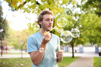 Photo of Young man blowing soap bubbles in park