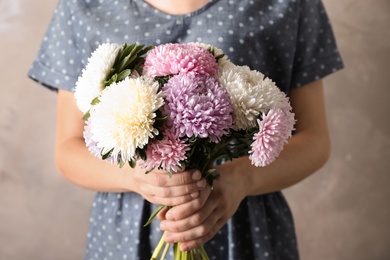 Woman holding beautiful aster flower bouquet against color background