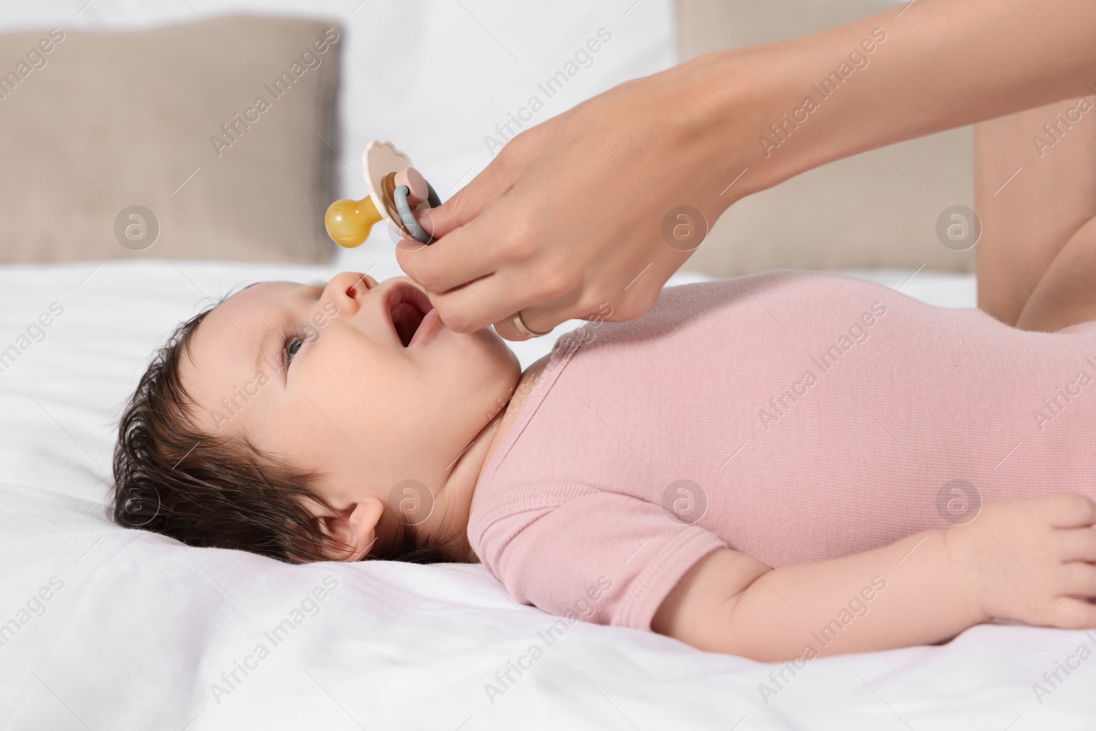 Photo of Mother giving pacifier to crying little baby on bed, closeup