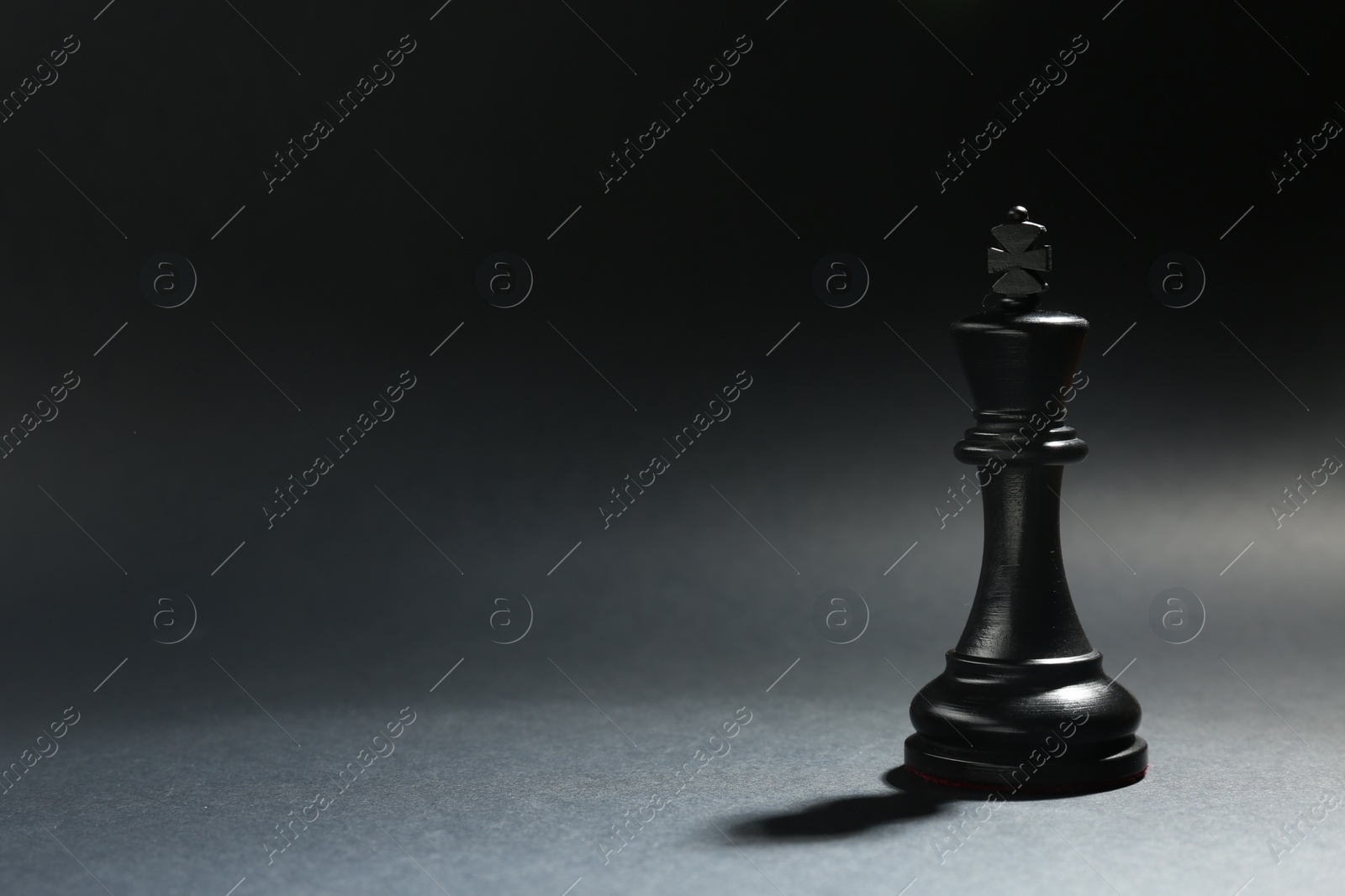 Photo of Black wooden chess king on dark background. Space for text