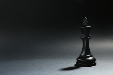Photo of Black wooden chess king on dark background. Space for text