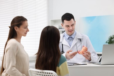 Photo of Gastroenterologist with model of stomach consulting woman and her daughter in clinic