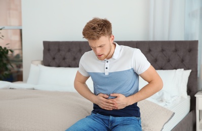 Photo of Young man having nausea in bedroom. Feeling  sick