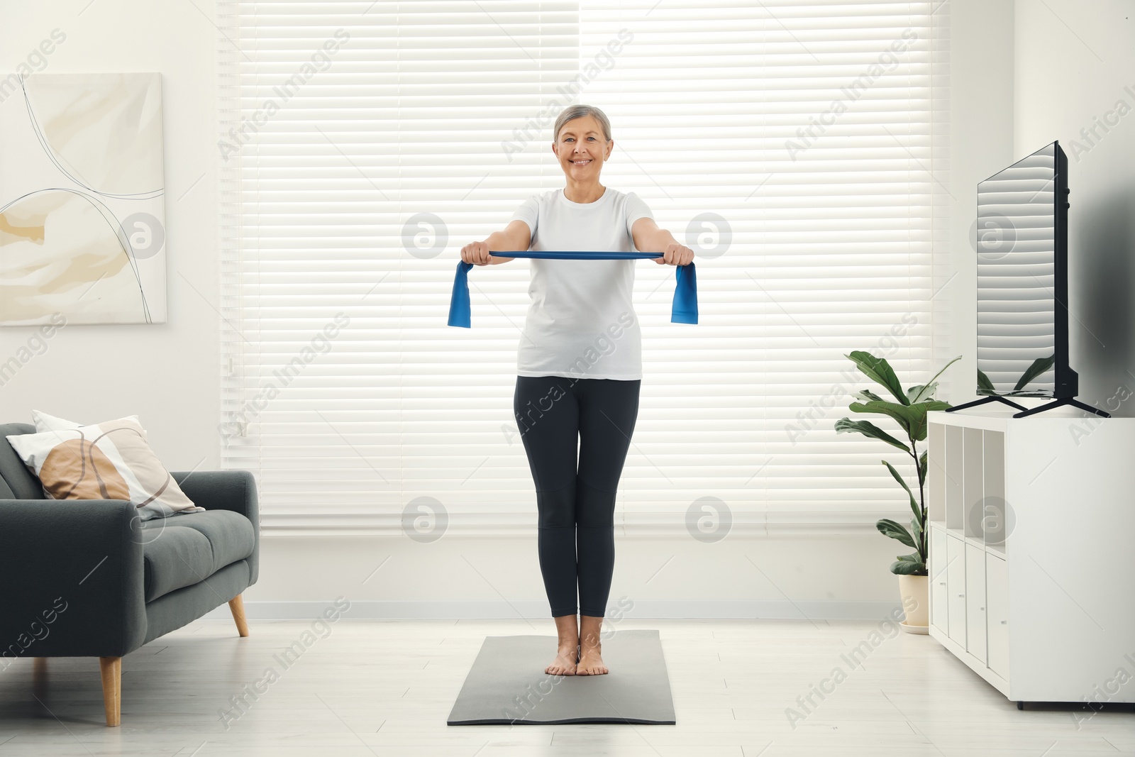 Photo of Senior woman doing exercise with fitness elastic band on mat at home