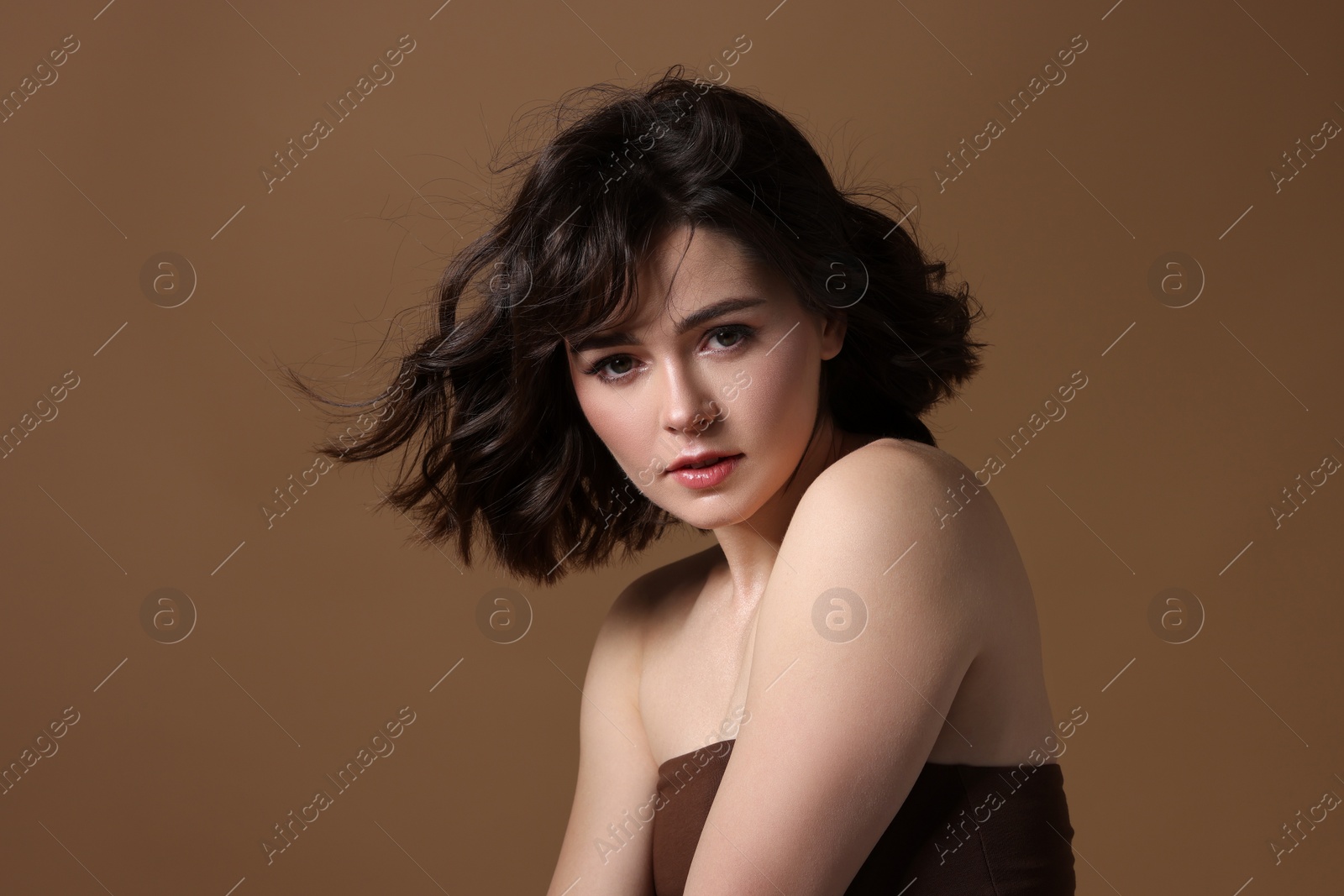 Photo of Portrait of beautiful young woman with wavy hairstyle on brown background