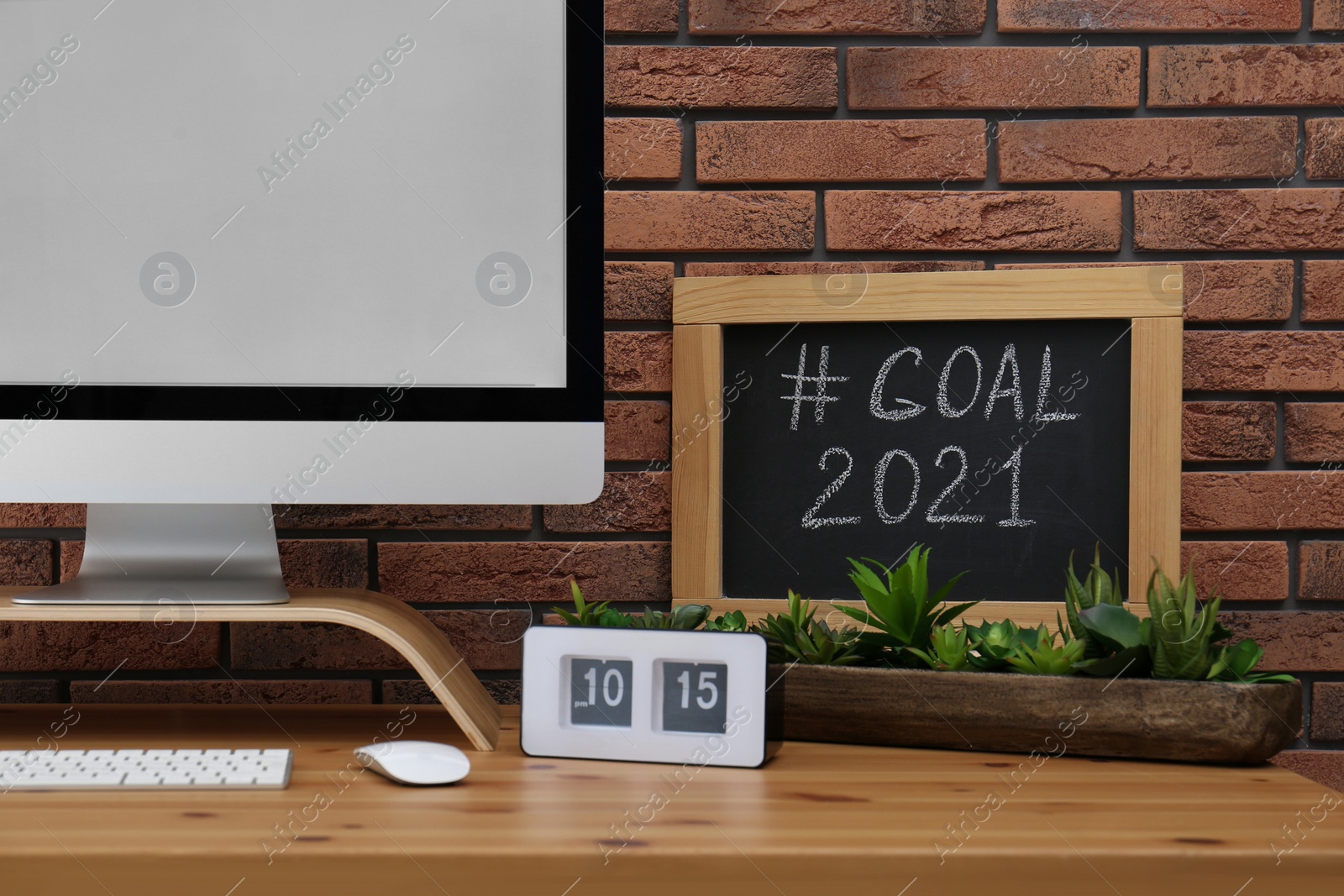 Photo of Blackboard with hashtag Goal 2021 near computer monitor on wooden desk in office