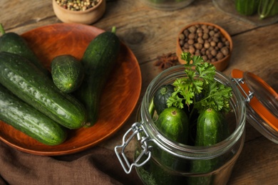 Photo of Pickling jar with fresh ripe cucumbers and spices on wooden table, closeup