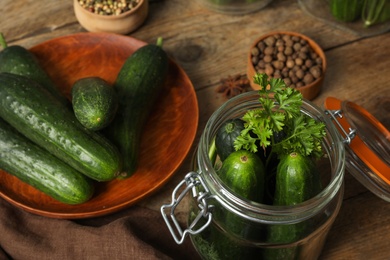 Pickling jar with fresh ripe cucumbers and spices on wooden table, closeup