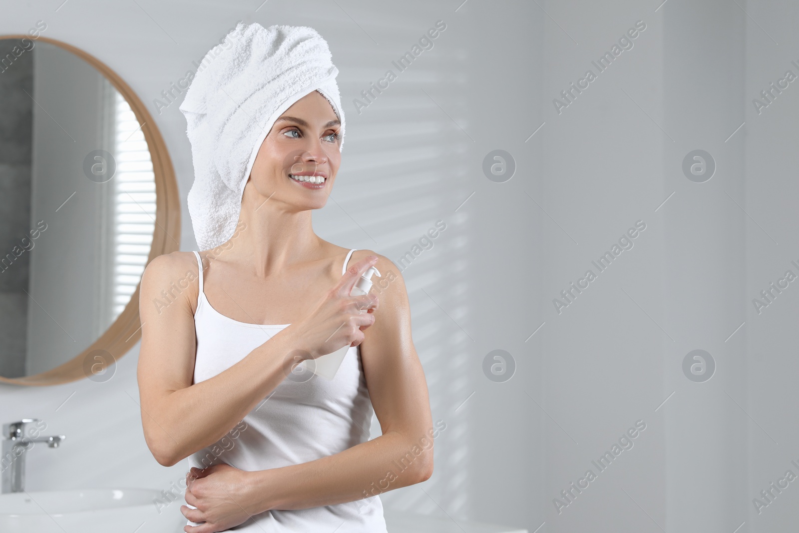 Photo of Happy woman applying body oil onto shoulder in bathroom, space for text