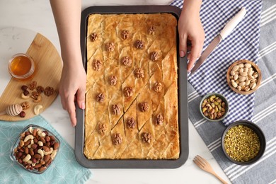 Photo of Woman with baking pan of delicious baklava at white table, top view