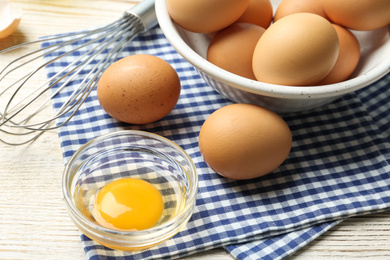 Photo of Chicken eggs and whisk on white wooden table, closeup