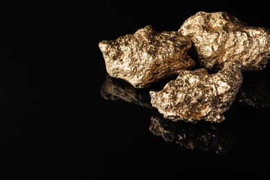 Photo of Gold nuggets on black reflective surface, space for text