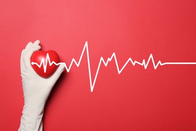 Doctor in medical glove holding heart on red background, top view