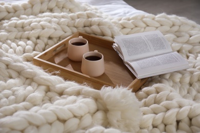 Photo of Wooden tray with cups and book on white knitted plaid