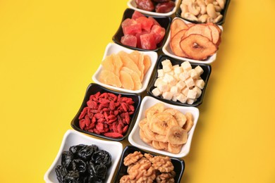 Photo of Bowls with dried fruits and nuts on yellow background