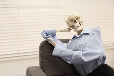 Photo of Waiting concept. Human skeleton sitting in armchair at office