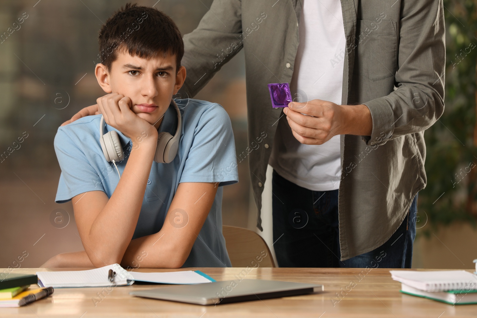 Photo of Father giving condom to his teenage son while he doing homework at home. Sex education concept