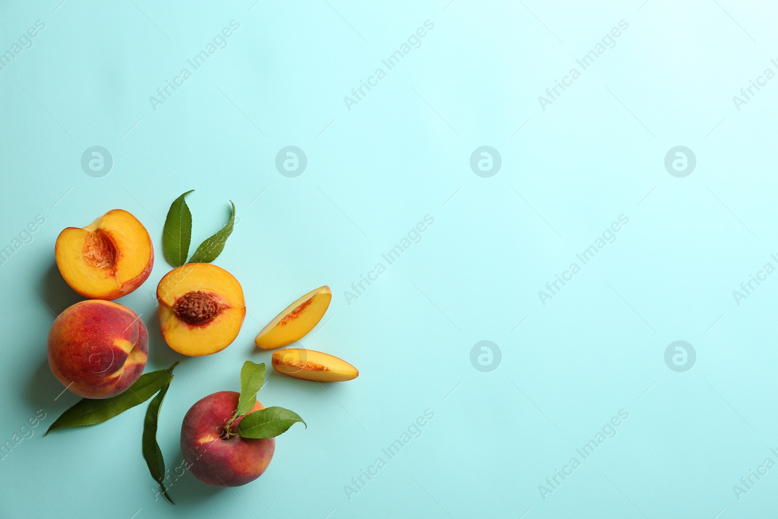 Photo of Fresh ripe peaches and green leaves on light blue background, flat lay. Space for text