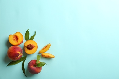 Photo of Fresh ripe peaches and green leaves on light blue background, flat lay. Space for text
