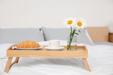 Bouquet of beautiful daisy flowers and breakfast on wooden tray in bedroom