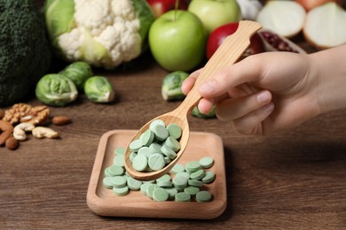 Photo of Woman holding spoon of pills at table with foodstuff , closeup. Prebiotic supplements
