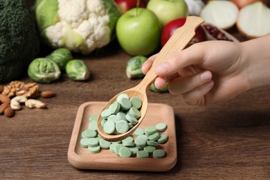 Woman holding spoon of pills at table with foodstuff , closeup. Prebiotic supplements