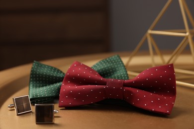 Photo of Stylish color bow ties and cufflinks on golden table, closeup