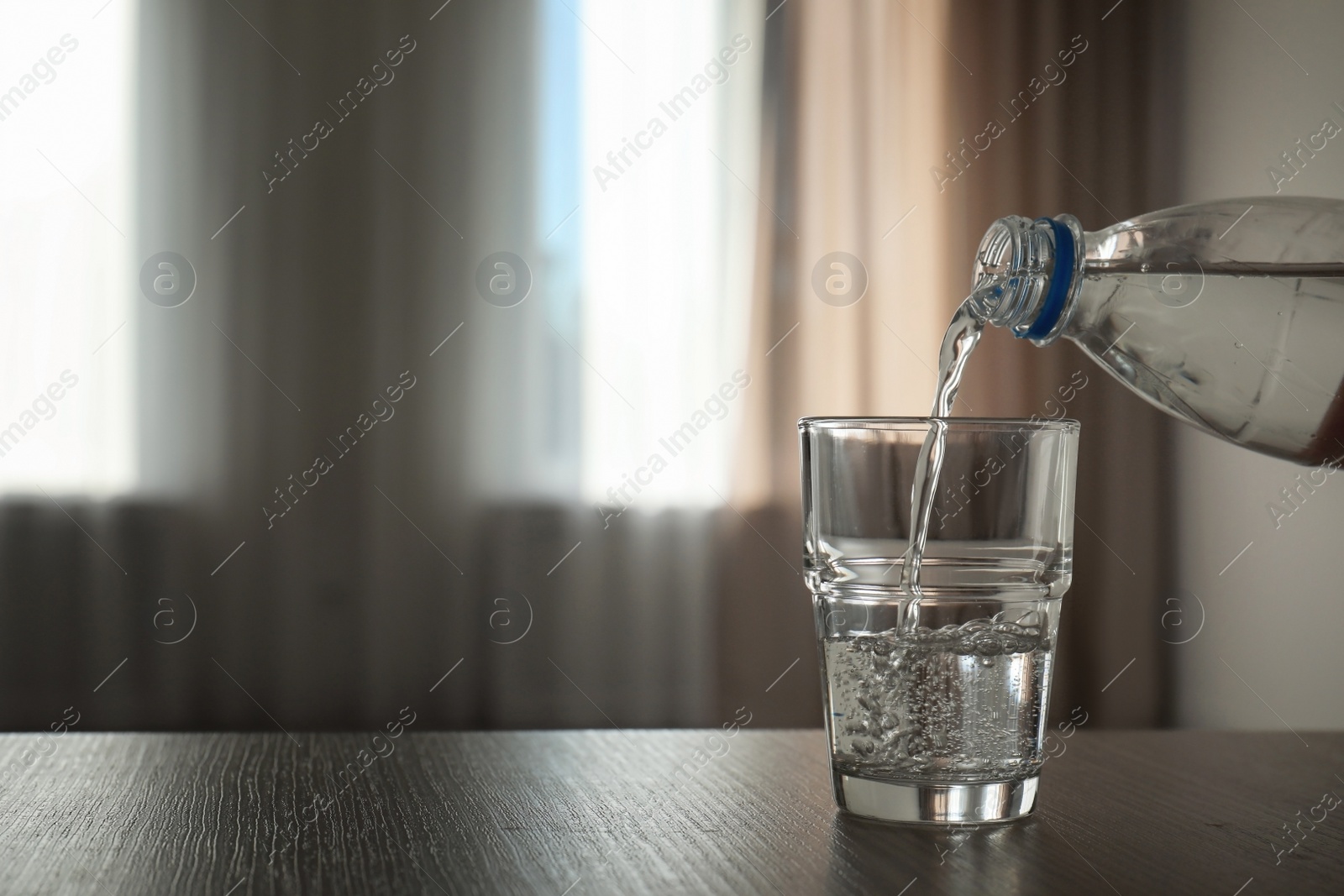 Photo of Pouring water from bottle into glass on blurred background. Space for text