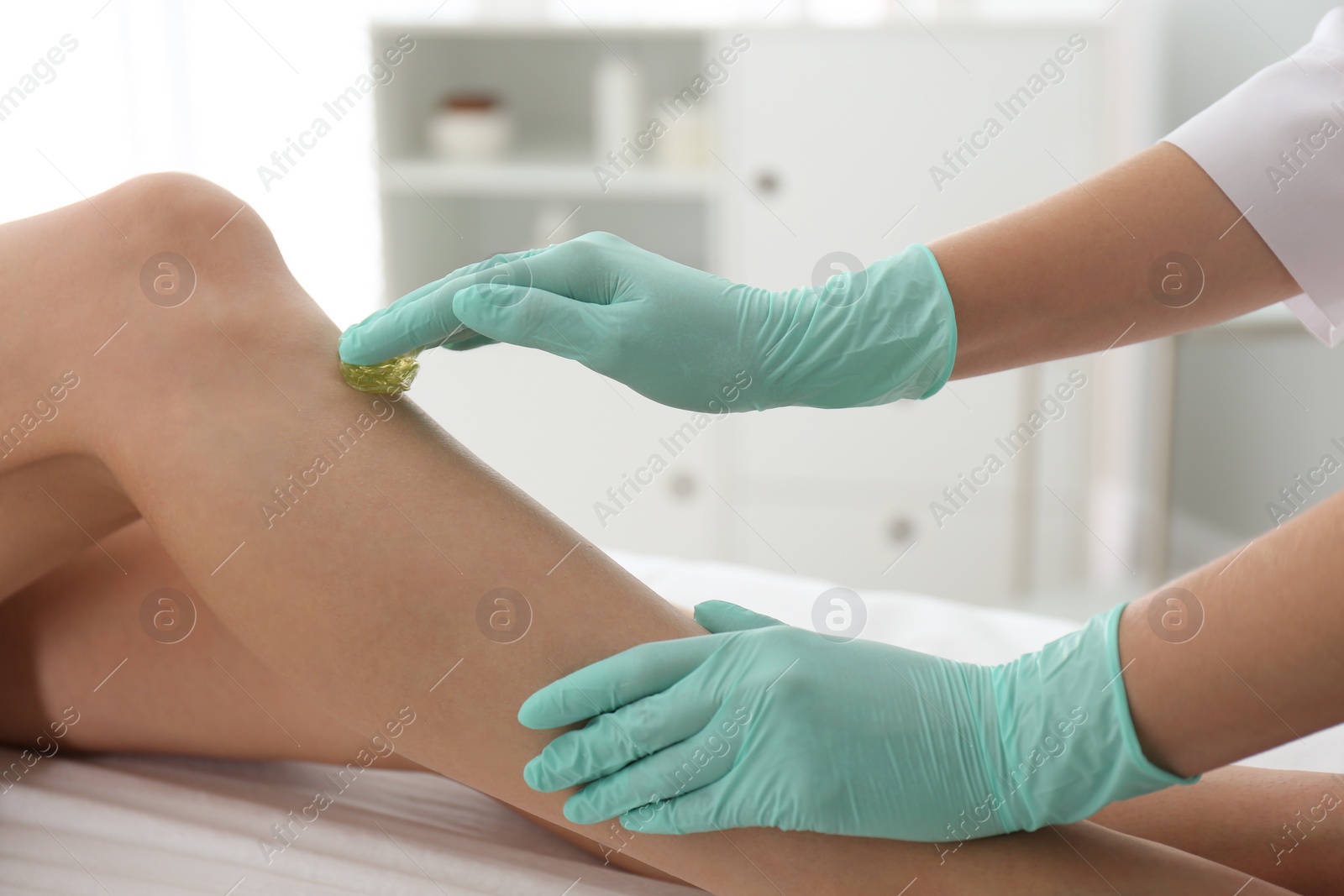 Photo of Woman getting wax epilation of legs in salon, closeup