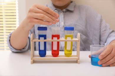 Photo of Girl with colorful liquids in test tubes and beaker at white table indoors, closeup. Chemical experiment set for kids