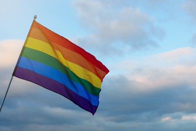 Photo of Bright LGBT flag against blue sky with clouds. Space for text