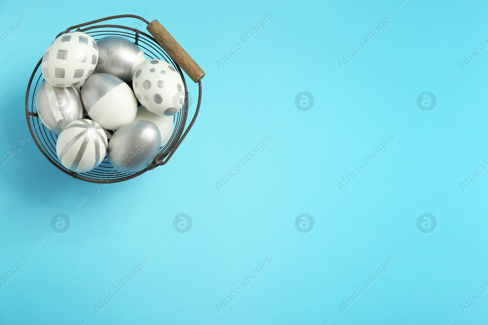 Photo of Basket full of painted Easter eggs on color background, top view. Space for text