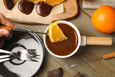 Photo of Woman dipping slice of orange into fondue pot with milk chocolate at wooden table, top view