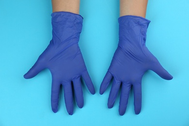 Person in medical gloves on light blue background, top view