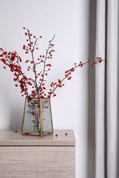 Photo of Hawthorn branches with red berries in vase on wooden table indoors