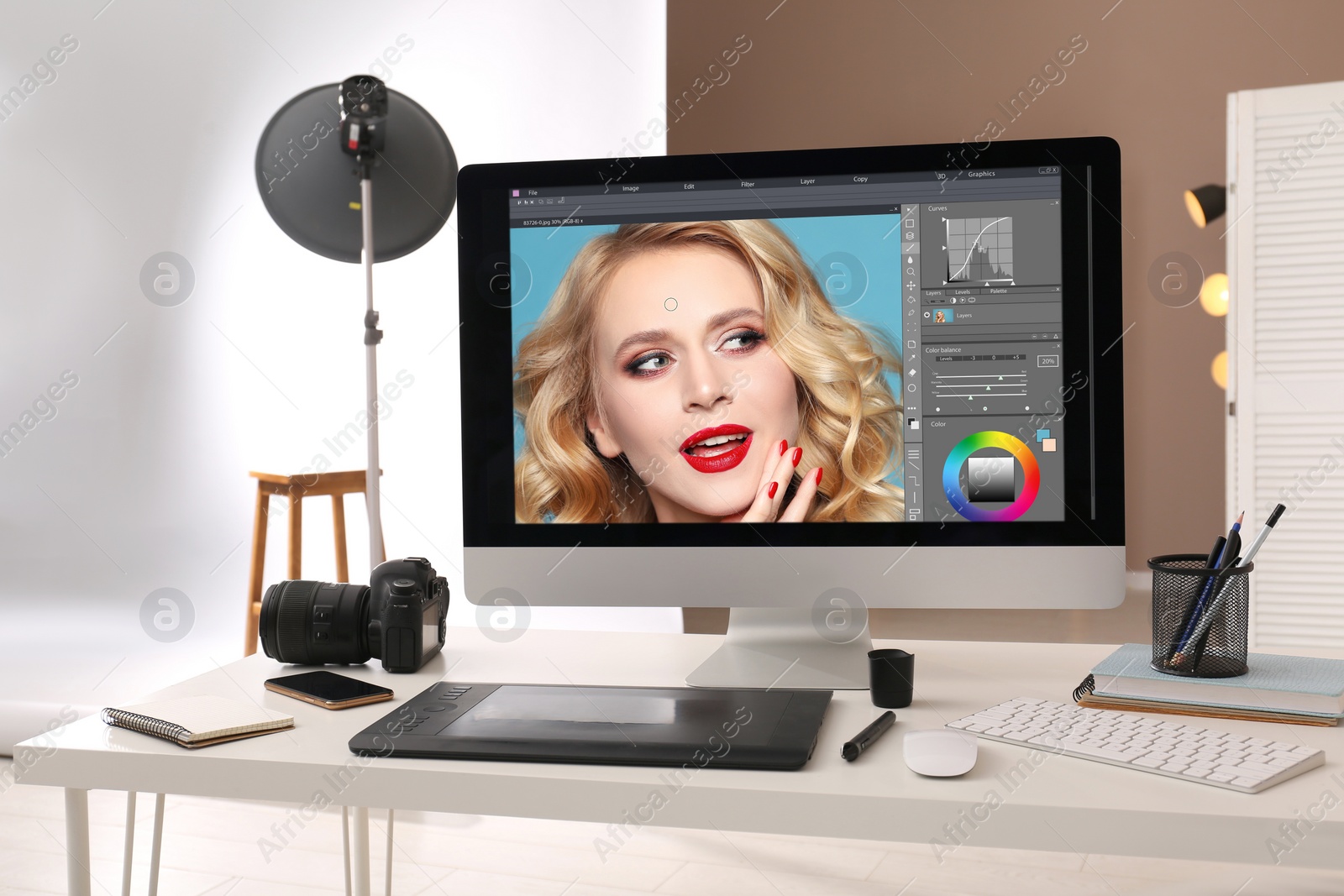 Photo of Retoucher's workplace. Computer with photo editor application, camera, smartphone and graphic tablet on table in studio