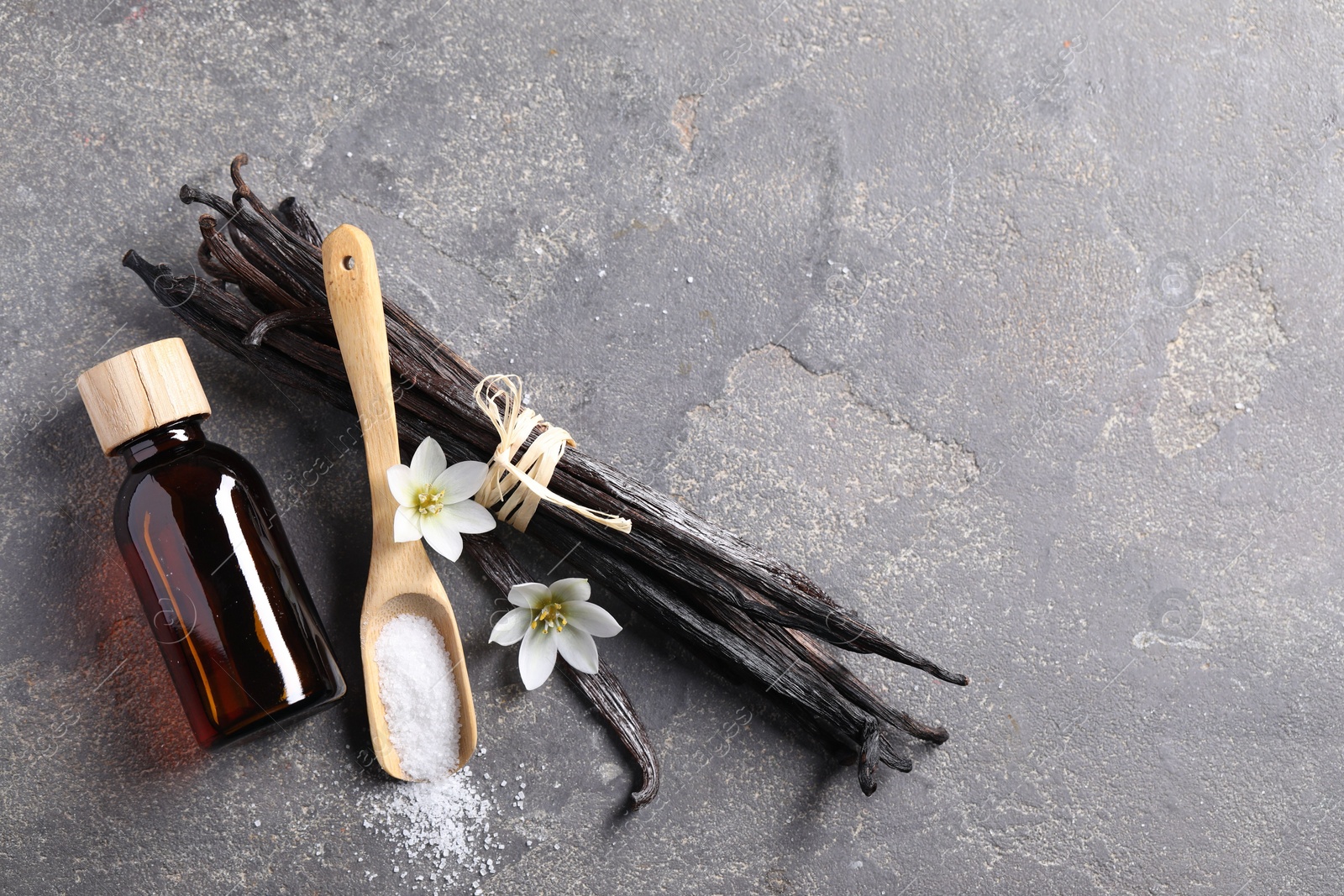 Photo of Spoon with sugar, flowers, vanilla pods and bottle of essential oil on grey textured table, flat lay. Space for text