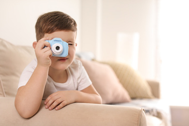 Photo of Little photographer taking picture with toy camera on sofa at home. Space for text