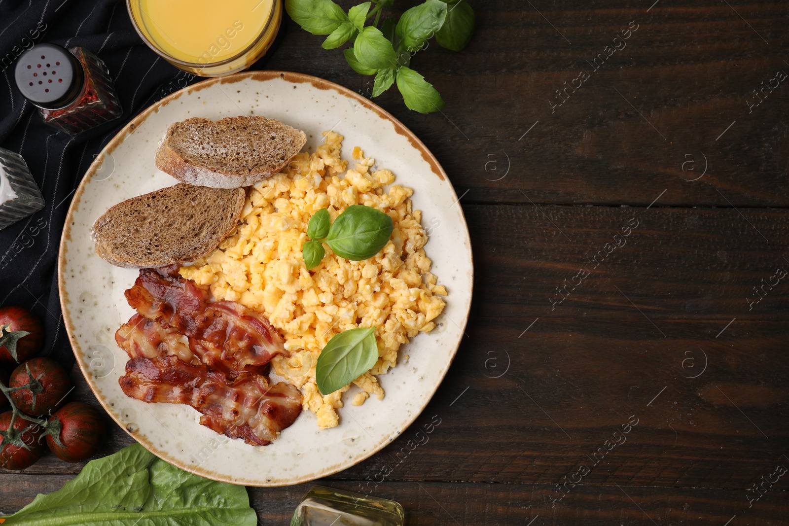 Photo of Delicious scrambled eggs with bacon and products on wooden table, flat lay. Space for text