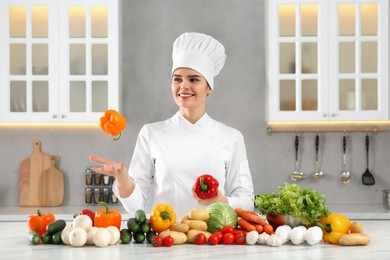 Photo of Happy chef throwing bell pepper near fresh vegetables at table in kitchen